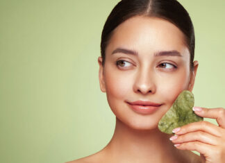 Hau(p)tsache glatt Frau hält einen Gua-Sha Massagestein aus Jade an ihre Wange