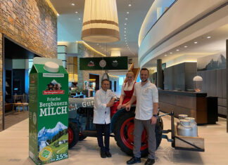 Kempinski Berchtesgaden: 20 Jahre gelebte Regionalität Übergroße Milchtüte Berchtesgardener Land in Hotellobby, mit drei Personen vor einem Traktor