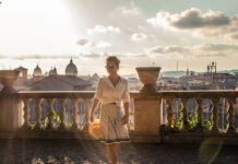 Salve Roma – Ein Besuch in der Ewigen Stadt Junge blonde Frau, sommerlich gekleidet auf einem antiken Balkon mit Aussicht über die Dächer von Rom