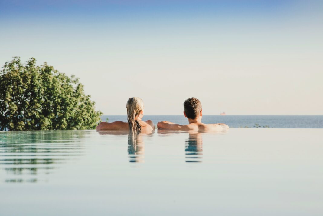 bearbeitet_Paar Eine Frau und ein Mann schauen vom Rand eines Infinity-Pools auf das Meer.