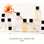 NOBILIS GROUP und Essential Parfums verkünden Vertriebspartnerschaft Gefüllte Flakons neben- und aufeinander angeordnet. Eine Gerbera mit orangefarbener Blüte ist dazwischen drapiert.