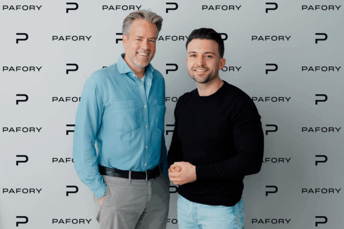 Zwei Männer stehen vor einer Wand mit Werbeaufdruck