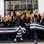 Sephora eröffnet ersten eigenen Store in München Mitarbeitende von Sephora, alle dunkel gekleidet, stehen mit einem Banner vor dem Shop