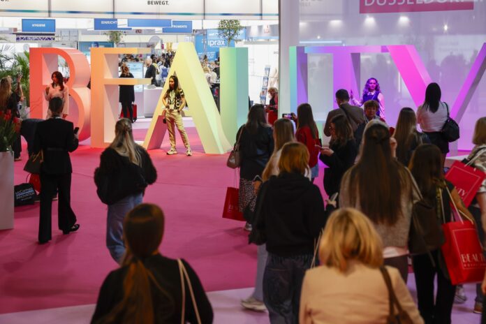 Messebesucher laufen über einen rosa farbenen Teppich zu den mannshohen Buchstaben des Beauty-Schriftzuges