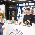 DUFTSTARS: Publikumspreis zum Anfassen Junger Mann in dunklem Shirt vor einem Regal mit vielen Duftflakons beim Beraten einer Kundin.