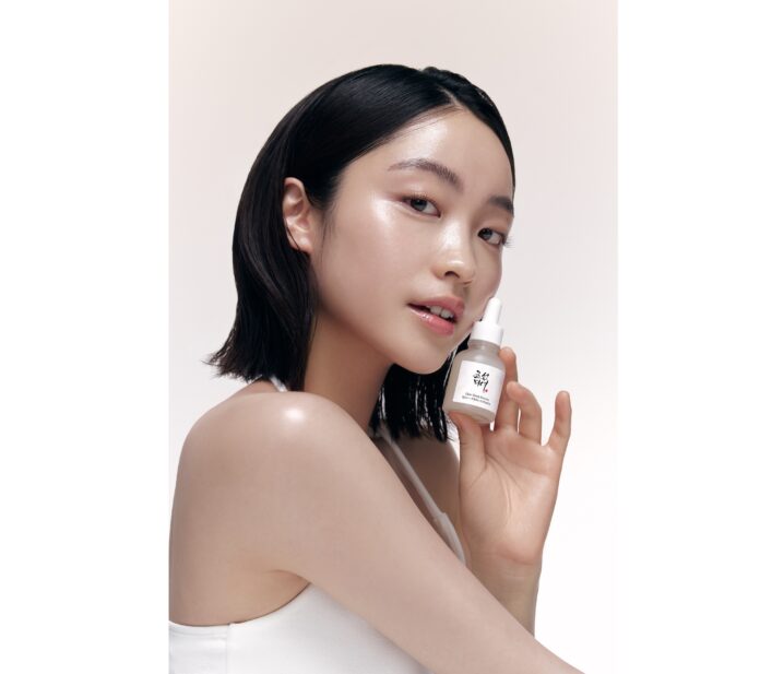 Eine junge Frau asiatischen Aussehehns hält ein Fläschchen mit Serum in der Hand.